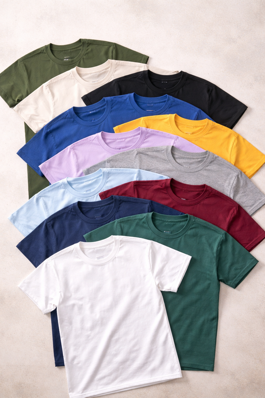 Flatlay of overlapping Gildan t-shirts arranged in a fan pattern, showing a range of neutral, green, blue, and warm accent colors.